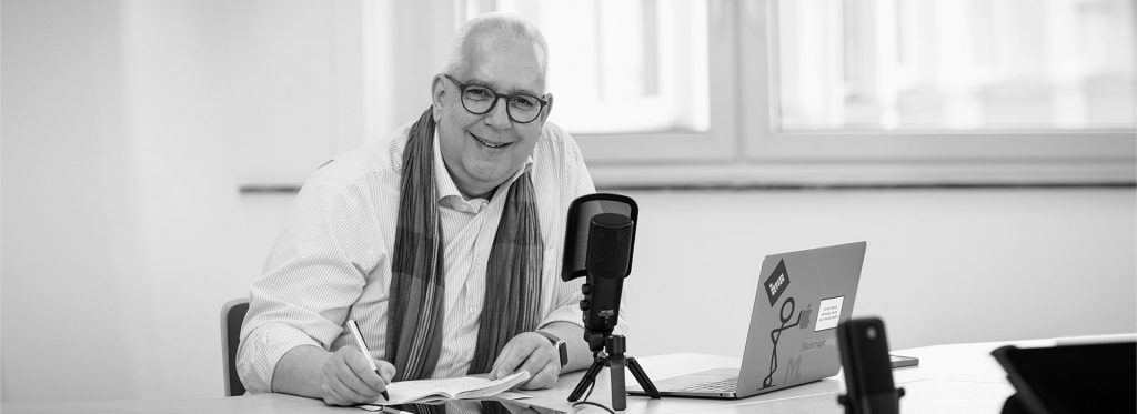 Frank Michna mit Stift am schreiben, neben ihm ein Mikrofon und Laptop